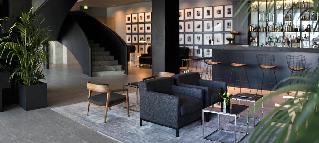 Mūsdienīgs viesnīcas vestibils ar elegantiem melniem un pelēkiem toņiem, ērtiem krēsliem un bāru, kas apgaismots ar stilīgām gaismām. Vieta ir dekorēta ar augiem un mākslas darbiem uz sienām.