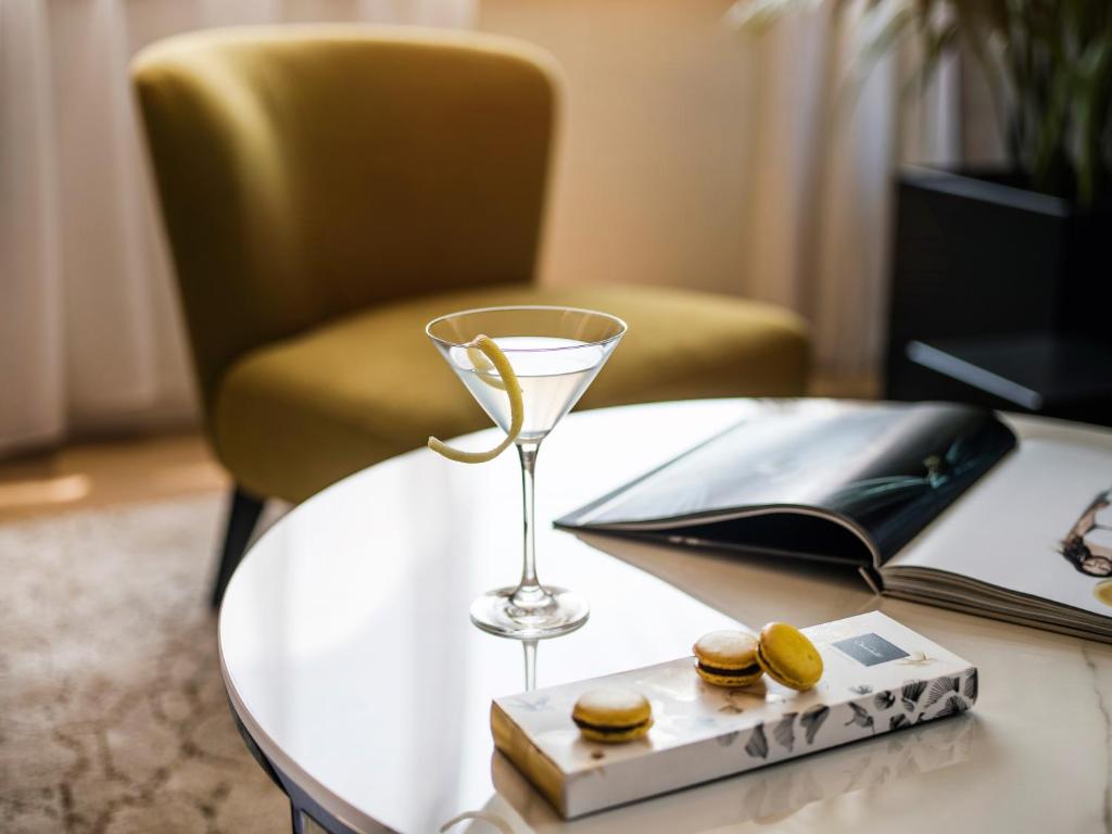 Elegants dzēriens ar citrona miziņu un makaronu kārumiem uz galda blakus žurnālam un dzeltenai krēslam.
