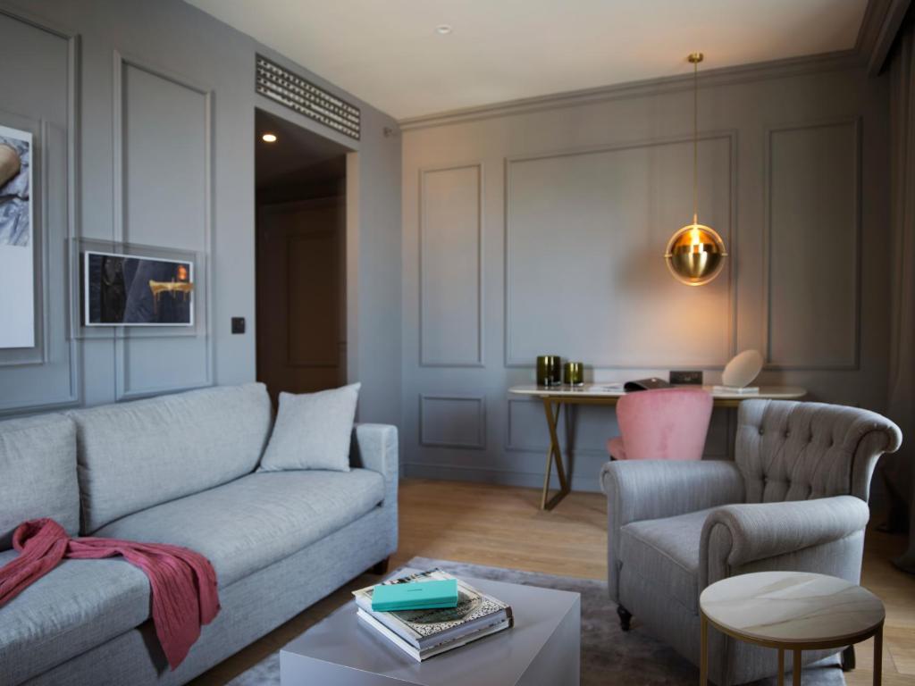 Mūsdienīga viesistaba ar pelēkām sienām, ērtiem mēbeļu komplektiem un elegantu apgaismojumu, kas rada siltu un aicinošu atmosfēru. Izcelts stils un komforts, ideāli piemērots relaksācijai vai darbam.