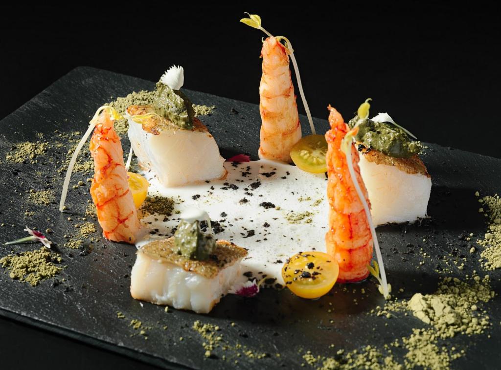 Eleganti uzlikts sushi ar garnelēm un zivi, pasniegts uz melnas akmens plāksnes, papildināts ar garšaugiem un dekoratīviem dārzeņiem.