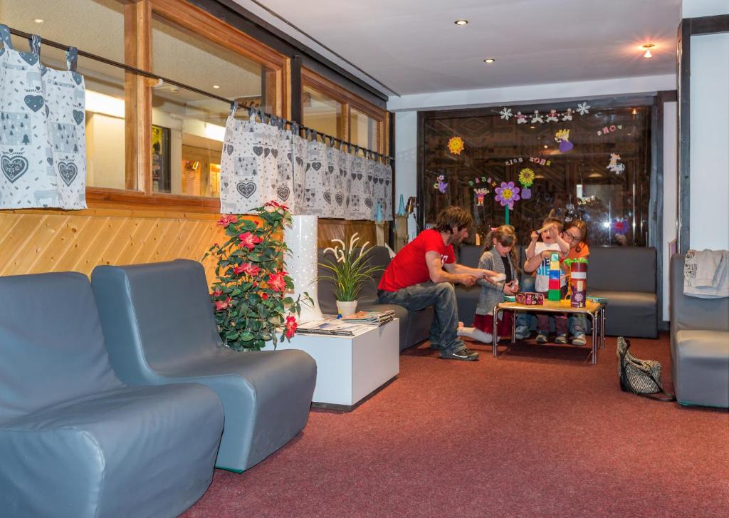 Bērnu aktivitātes telpa, kur pieaugušais palīdz bērniem spēlēt spēles, apkārt ir ērtas mēbeles un dekoratīvi elementi.