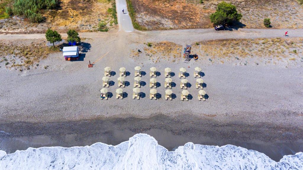 Pludmales ainava ar saules krēslu rindām un viļņiem, kas sitas krastā. Skats no augšas uz pludmales kafejnīcu un pastaigu ceļu.