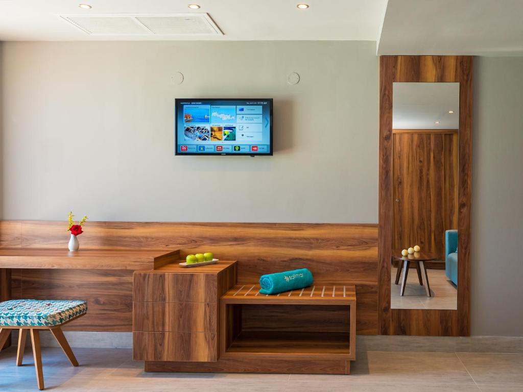 Mūsdienīgs viesnīcas numura interjers ar koka mēbelēm, televizoru pie sienas un dekoratīvu puķu vāzi. Gaismas toņi un eleganta dizaina elementi rada viesmīlīgu atmosfēru.