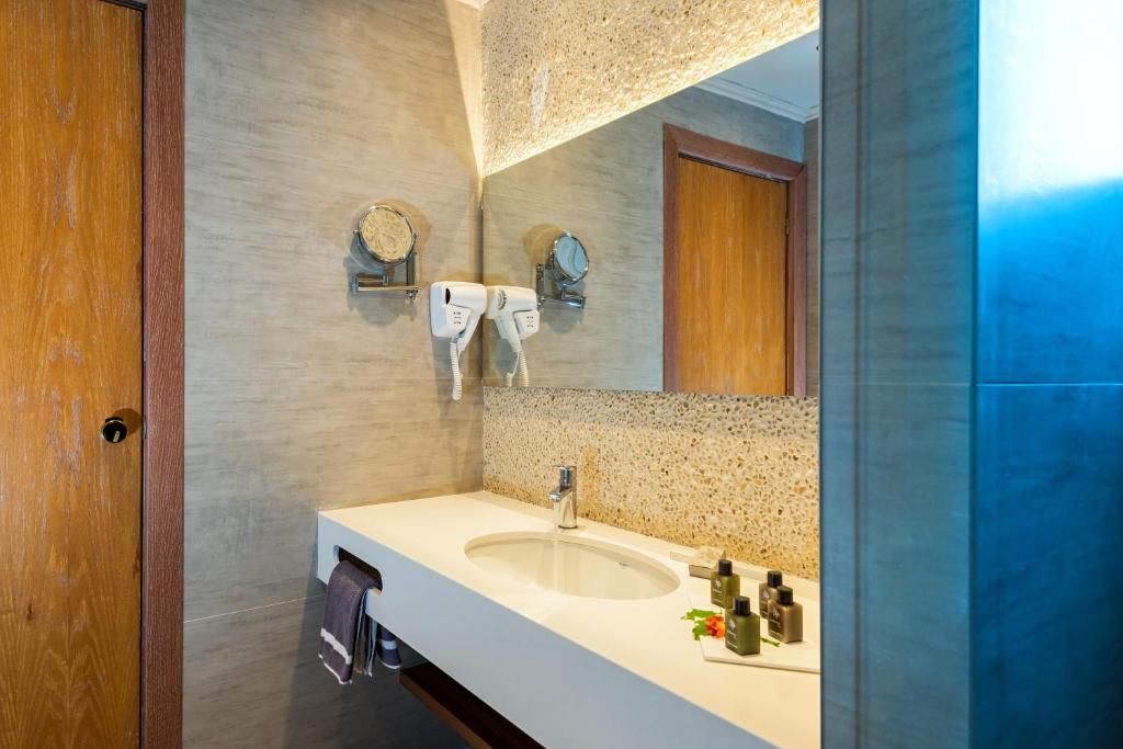 Mūsdienīgs vannas istabas interjers ar gaišu krāsu paleti, izsmalcinātu izlietni un dekoratīviem elementiem, piemēram, augu izstrādājumiem un matu fēniem.