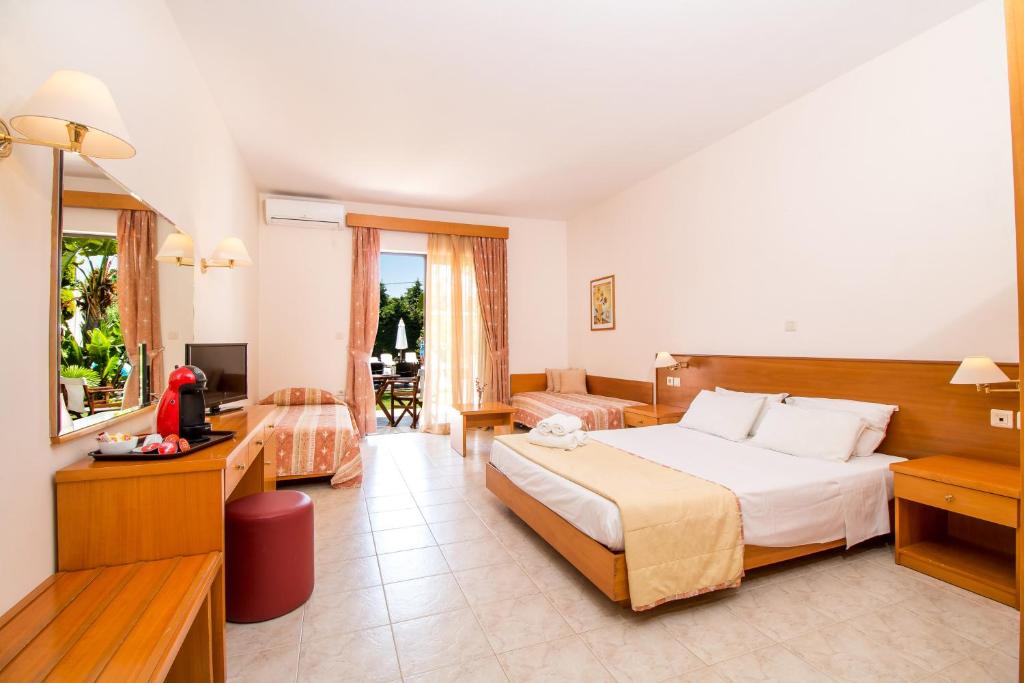 Gaiša viesnīcas istaba ar divām gultām un atpūtas zonu, kurā ir televizors un kafejnīcas automāts. Logi ved uz dārzu ar terasi, radot patīkamu atmosfēru.