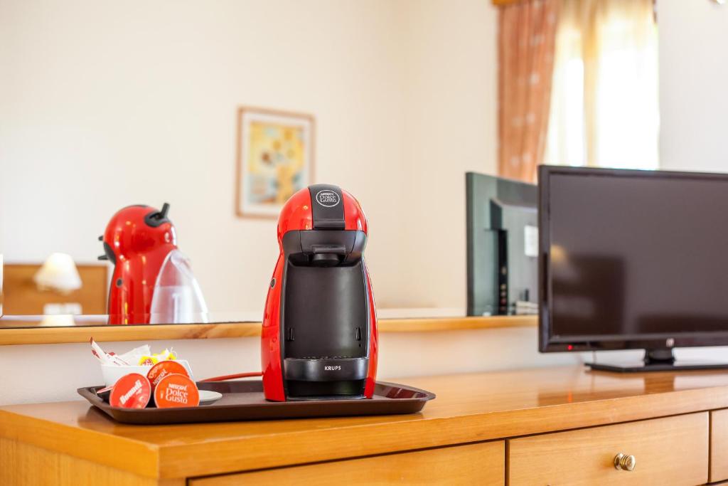 Sarkana kafijas automāta iekārta un televizors uz koka galda viesnīcas numurā, ar atspīdumu spogulī.