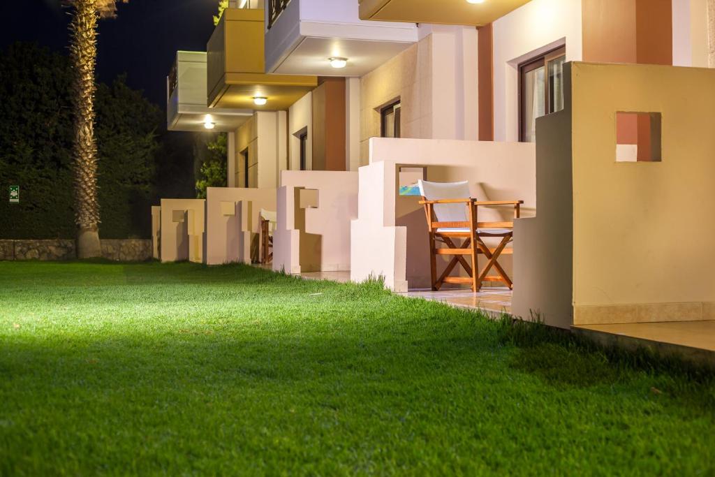 Nakts ainava ar zālienu un balkoniem, kas aprīkoti ar koka krēsliem, piedāvā mierīgu un relaksējošu atmosfēru. Gaisma apgaismo apkārtni, radot siltu noskaņu.