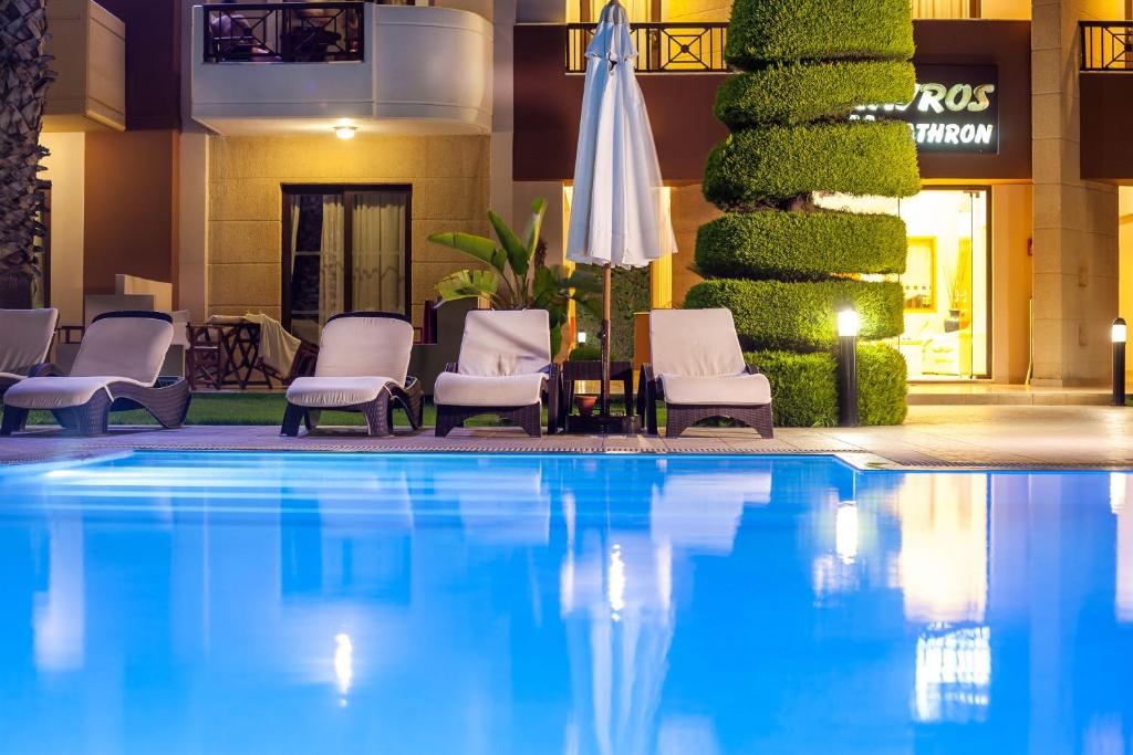 Peldbaseins ar zilu ūdeni un atpūtas krēsliem, apzaļumots stūris un apgaismojums, kas rada relaksējošu atmosfēru.