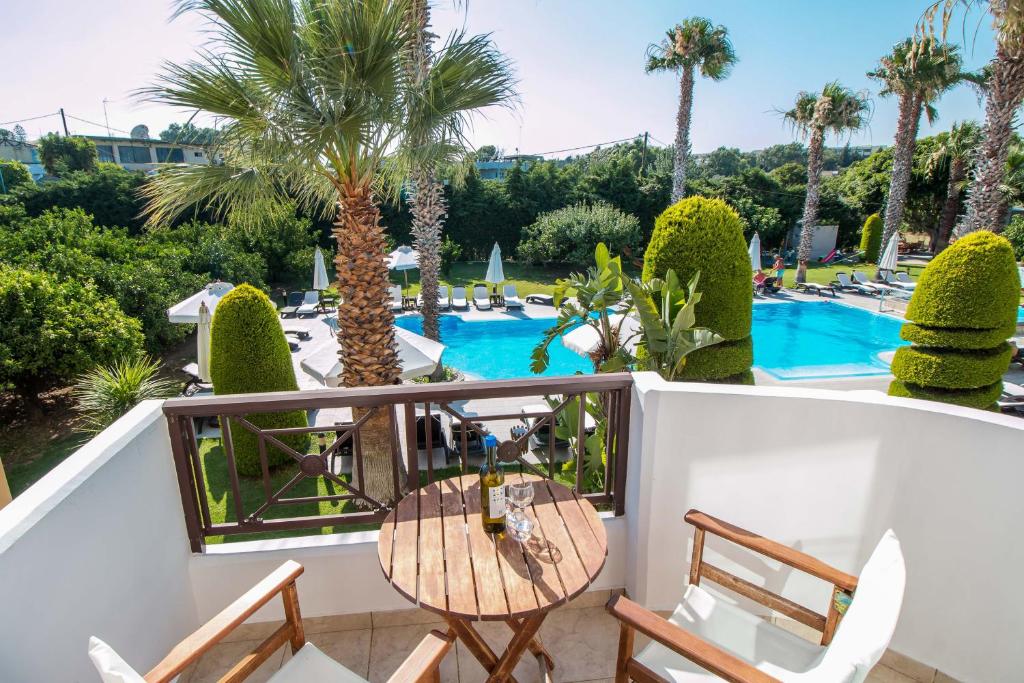 Balkons ar skatu uz baseinu, kurā ir palmām un zaļumiem ieskauts atpūtas laukums. Uz galda novietota pudele ar vīnu un glāze.