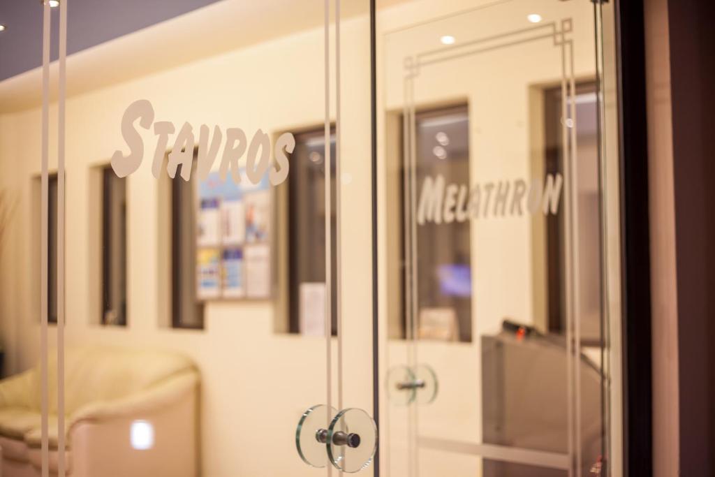 Stikla durvis ar nosaukumiem "Stavros" un "Melathron" uz gaiša fona, kas rada modernu un elegantu atmosfēru.