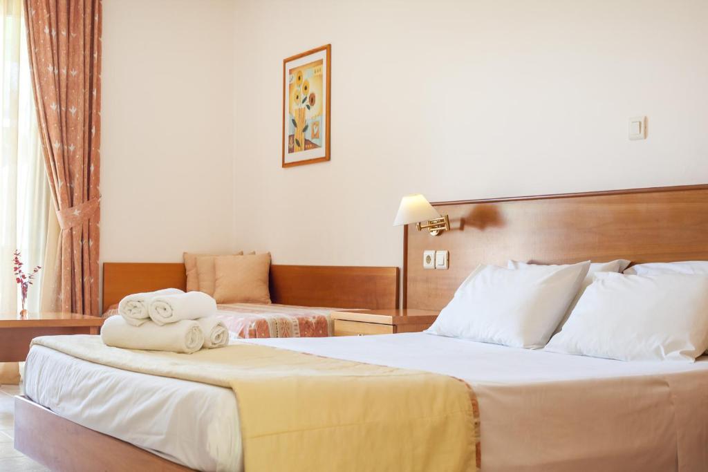 Gaišs viesnīcas numurs ar divām gultām, koka mēbelēm un logiem ar aizkariem. Uz gultas sakrāmēti dvieļi un blakus novietota dīvāna zona.