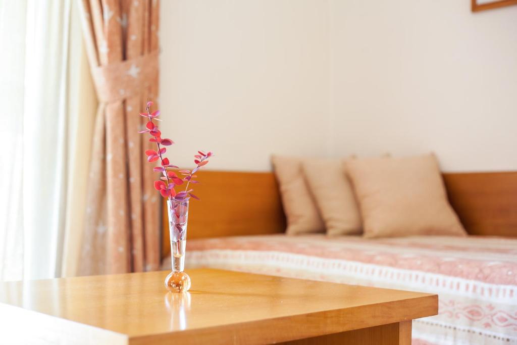 Skaista istaba ar koka galdu, uz kura novietots ziedu pušķis caurspīdīgā vāzē. Fons ietver gultu ar spilveniem un aizskarus, kas piedod mājīgu atmosfēru.