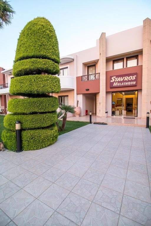 Viesnīcas ieeja ar stilīgu zaļo augu kompozīciju un modernu arhitektūru. Redzama nosaukuma zīme "Stavros Melathron".