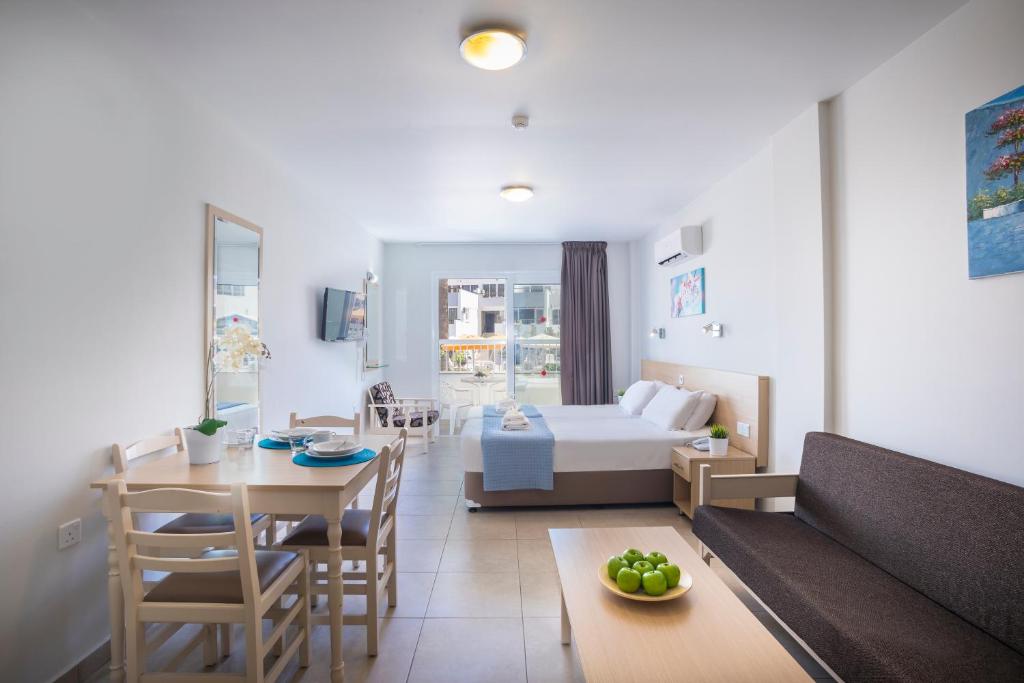 Mūsdienīgs viesnīcas numurs ar viesistabu un guļamistabu, kurā ir gaismas toņi, koka mēbeles un balkons. Uz galda novietotas trīs zaļas āboli un galda piederumi.