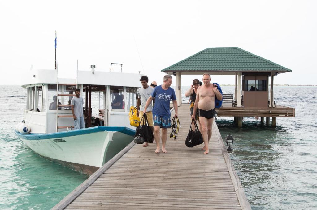 Cilvēki iznāk no laivas uz piestātni, nēsājot somas ar snorkelēšanas aprīkojumu. Apskate ir jūras ainava ar mierīgu ūdeni un nelielu būdiņu piestātnē.