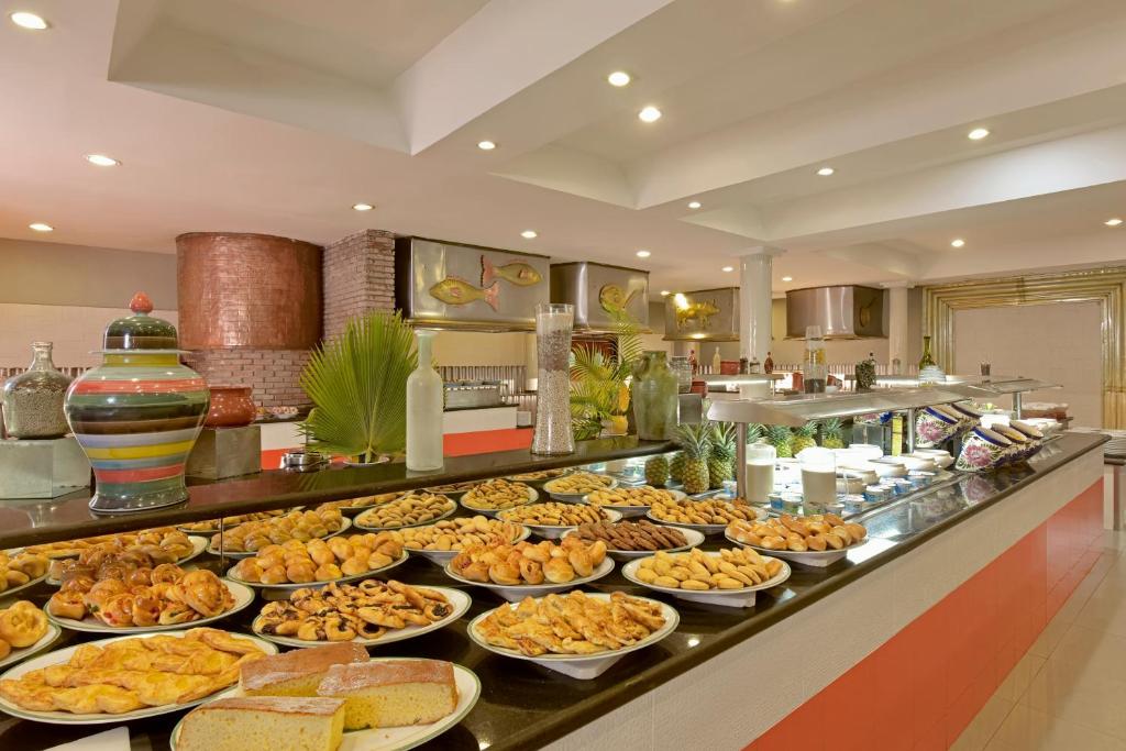 Bagātīgs bufetes galds ar dažādiem konditorejas izstrādājumiem un desertiem, kas pasniegti elegantā restorānā. Uz galda atrodas arī dekoratīvas trauku un augļu kompozīcijas.