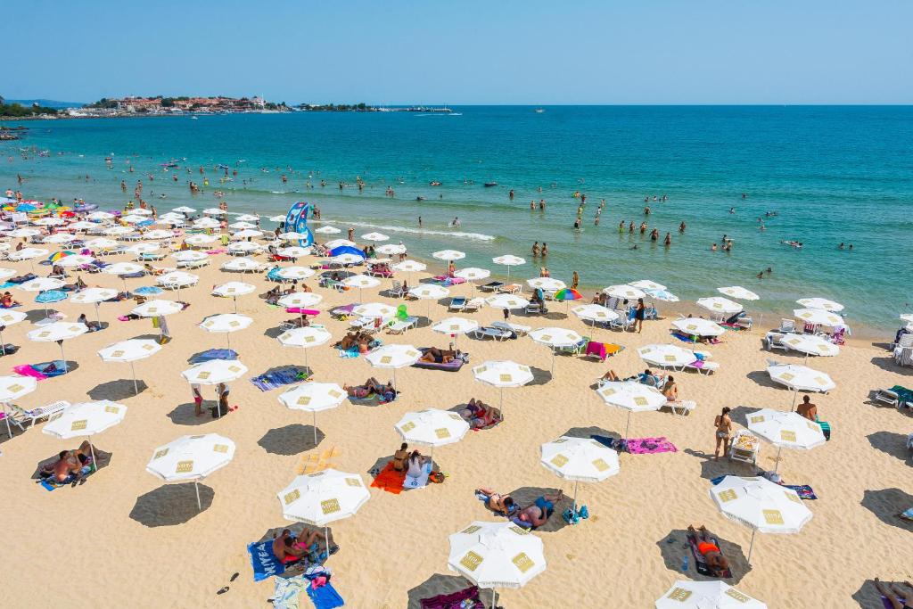 Pludmales skats ar saulessargiem un cilvēkiem, kas atpūšas pie ūdens. Jūras viļņi un peldētāji rada relaksējošu atmosfēru.