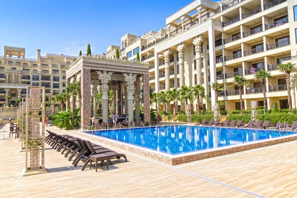 Luksusa viesnīcas peldbaseins ar palmām un ērtām sauļošanās krēsliem, apkārtne ar elegantām arhitektūras detaļām. Ideāla vieta relaksācijai un atpūtai.