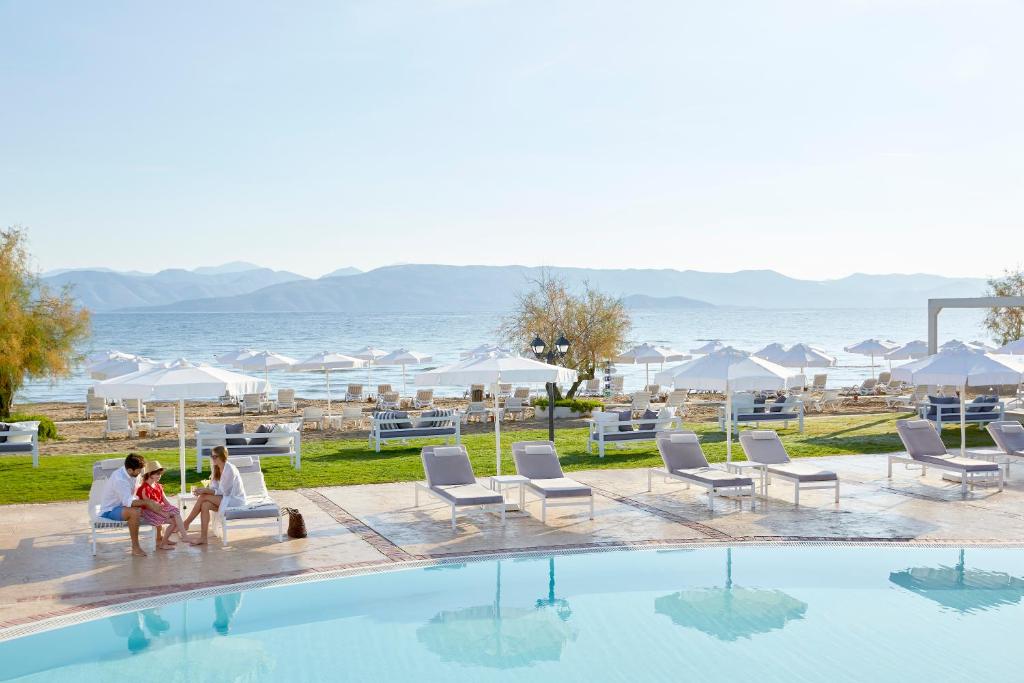 Viesnīcas pludmales zona ar baseinu un saules krēsliem, kurās atpūšas cilvēki, fons ar jūru un kalniem. Ideāla vieta relaksācijai un atpūtai.