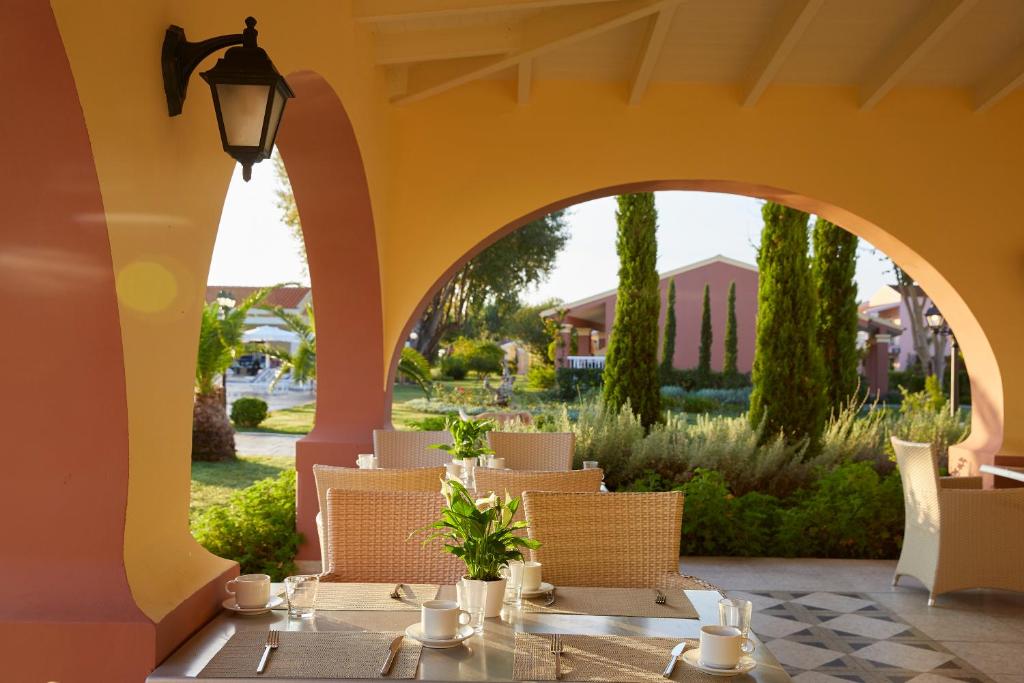 Terase ar elegantu galdu un krēsliem, kas piedāvā skatu uz zaļo dārzu un apkārtni. Gaisma plūst caur arku, radot siltu un viesmīlīgu atmosfēru.