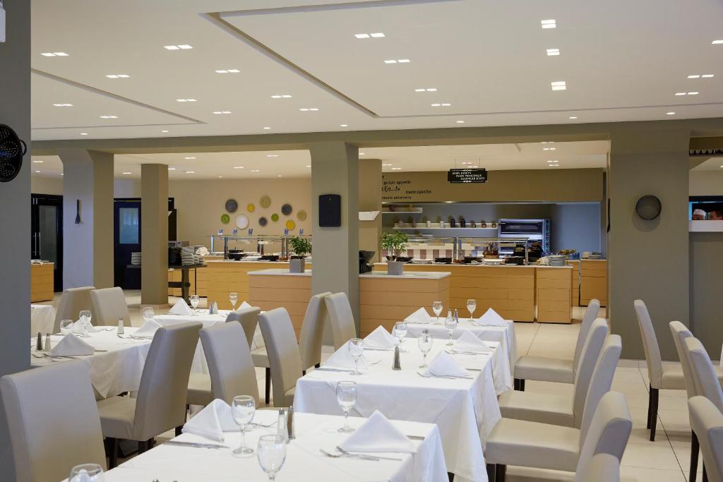 Mūsdienīgs restorāna interjers ar gaišām krāsām, elegantiem galdiem un labi sakārtotu virtuvi. Gaismas apgaismojums rada patīkamu atmosfēru.