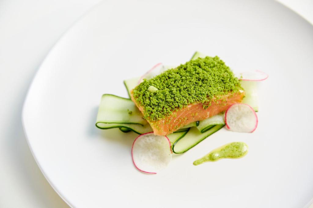 Svaiga laša fileja ar zaļo garšaugu pārklājumu, pasniegta uz gurķu un redīsu gultas ar zaļo mērci.