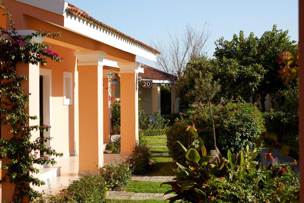 Kāds jauks dārza ainavas skats ar krāsainām mājām un zaļumiem. Redzamas ziedu krūmi un labi kopts zāliena stūris.