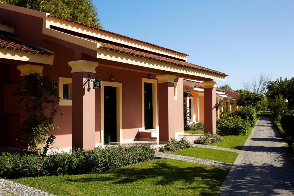 Mājas ar rozā sienām un zaļu zāli, apstādinātas gleznainā ainavā. Tuvumā redzama bruģēta taka, kas ved cauri dārziem.