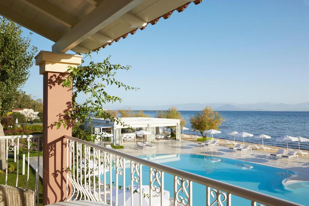 Skats uz baseinu un jūru no balkona, ar saulainu laiku un vasarīgu atmosfēru. Apkārt ir sauļošanās krēsli un balti saulessargi.