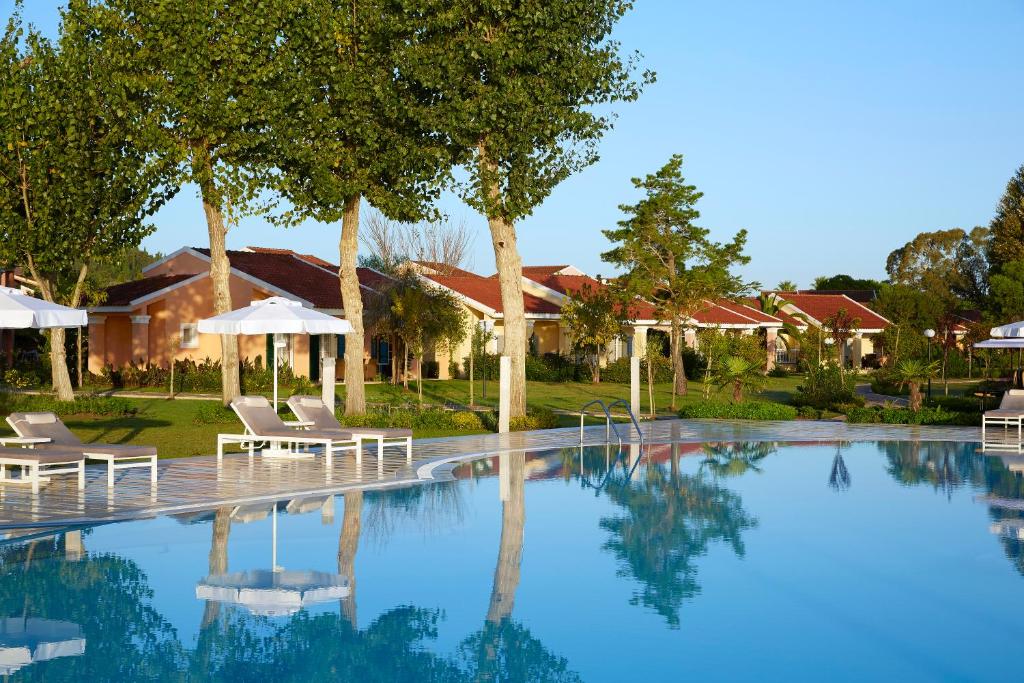 Kopiena ar skaidru baseinu un saulessargiem, kas atrodas dārzā blakus mājām ar sarkanu jumtu. Skaista laika apstākļu ainava ar zaļām lapām un zilo debesu fonu.