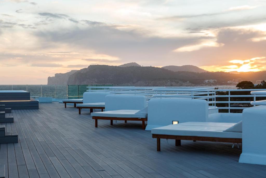 Terases skats ar baltām guļamvietām, kas vērstas uz jūru un kalniem, saulrieta gaismā.