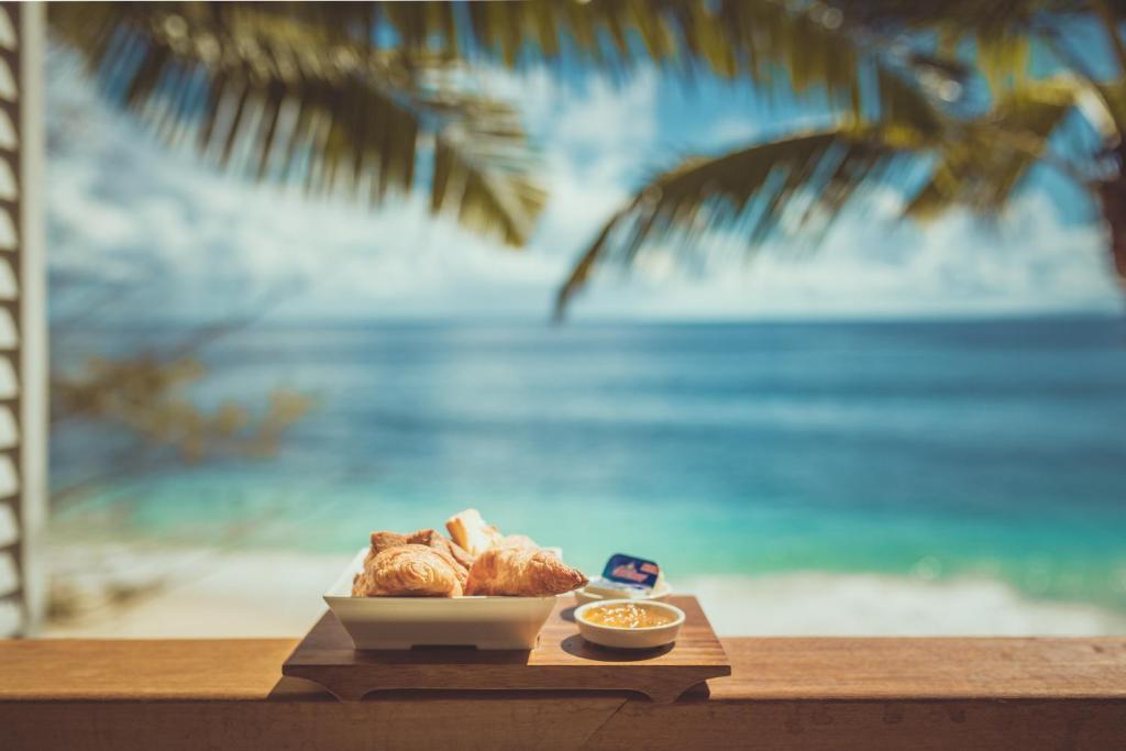 Gards brokastu galds ar kruasāniem un mērci, fons ar pludmales skatu un palmām.