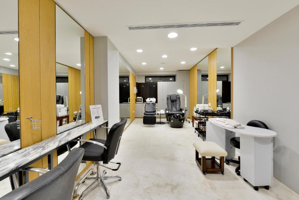 Mūsdienīgs skaistumkopšanas salons ar stilīgu interjeru, kurā redzami spoguļi, krēsli un darba virsmas. Telpa ir gaiša un plaša, radot relaksējošu atmosfēru.