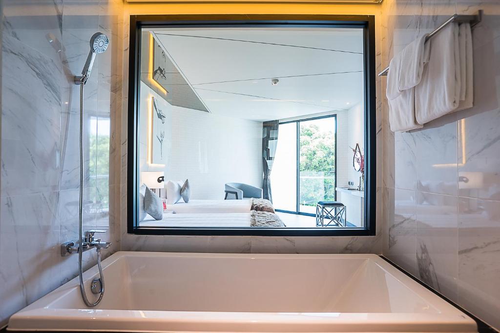Mūsdienīgs vannas istabas interjers ar lielu logu, kas sniedzas uz guļamistabu, radot atvērtu un gaisīgu atmosfēru. Vanna, dušas kabīne un moderns apgaismojums papildina kopējo estētiku.