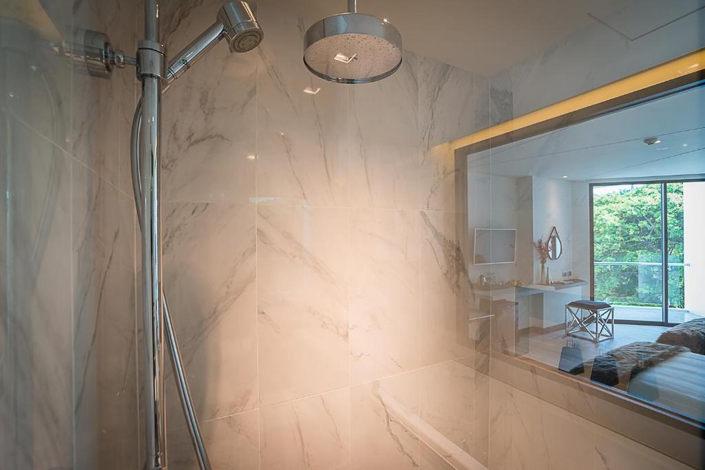 Mūsdienīga vannas istaba ar stikla dušu un elegantu marmora apdari, kas nodrošina gaisīgu un stilīgu atmosfēru. Skats uz blakus esošo istabu ar dabu caur logu.