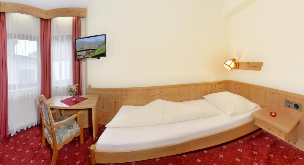 Mājīgs viesnīcas numurs ar vienguļamo gultu, koka mēbelēm un televizoru. Telpā ir arī galds ar ziediem un sarkana paklāja grīda.