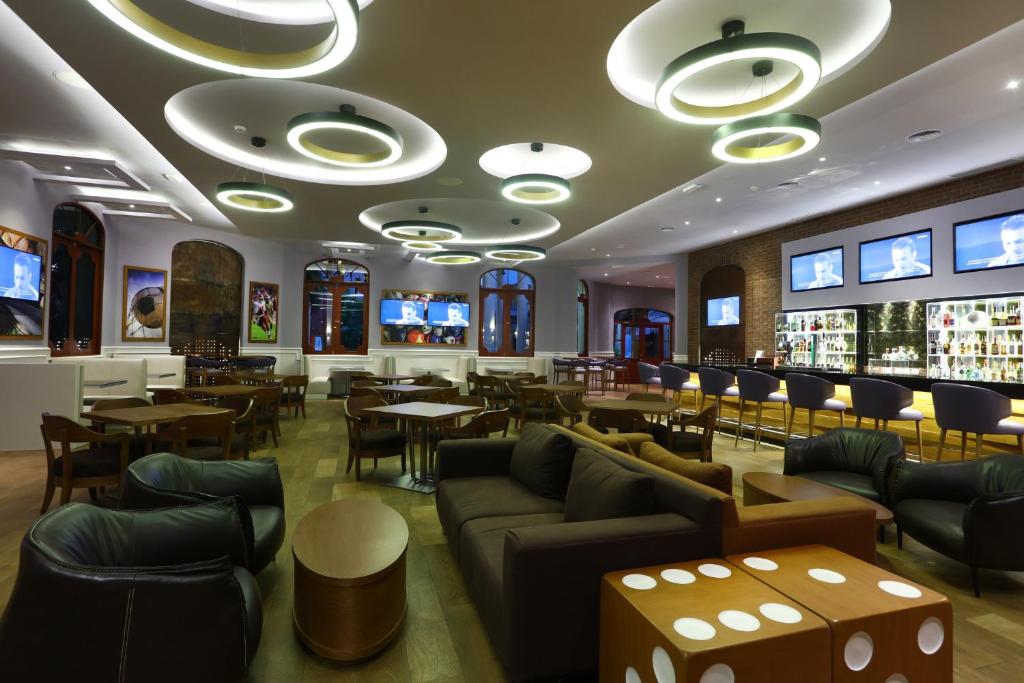 Mūsdienīga bāra interjers ar stilīgu apgaismojumu, ērtām mēbelēm un televizoriem, kas rāda sporta pārraides. Telpa ir plaša un aicinoša, ideāla relaksācijai vai izklaidei.