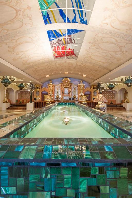 Luksusa pirts ar elegantu dizainu, kurā ir garš baseins ar mirdzošām flīzēm un krāšņām lampām. Griestos ir krāsains vitrāžas logs, kas piešķir telpai unikālu atmosfēru.