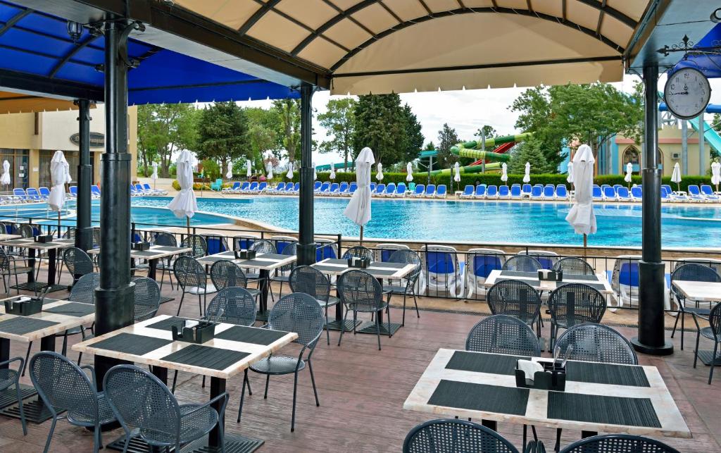 Restorāna terase ar skatu uz baseinu, kurā ir sēdvietas un sauļošanās krēsli. Apgaismojums un ainava rada relaksējošu atmosfēru.