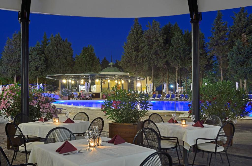 Elegants restorāns ar skatu uz baseinu, apgaismots naktī ar ziediem un skaistiem kokiem apkārt. Ideāla atmosfēra romantiskām vakariņām.