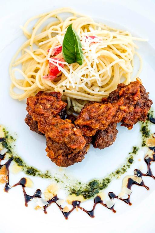 Pasta ar tomātu mērci un rīvētu sieru, pasniegta kopā ar ceptām gaļas bumbām un dekorēta ar zaļumiem un balzamiko redukciju.