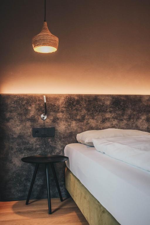 Mūsdienīga guļamistaba ar siltu apgaismojumu, kurā redzams gultas stūris, melns galdiņš un dekoratīva lampa.