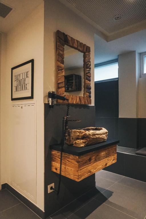 Mūsdienīgs vannas istabas dizains ar koka spoguli, akmens izlietni un melnu virsmu. Interjers apvieno dabīgas un mūsdienīgas estētikas elementus.