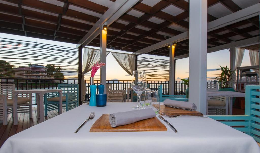 Restorāna terase ar eleganti uzklātu galdu, ziedu dekorāciju un panorāmas skatu uz saulrietu. Mūsdienīgs interjers ar gaišām krāsām un komfortablām mēbelēm.