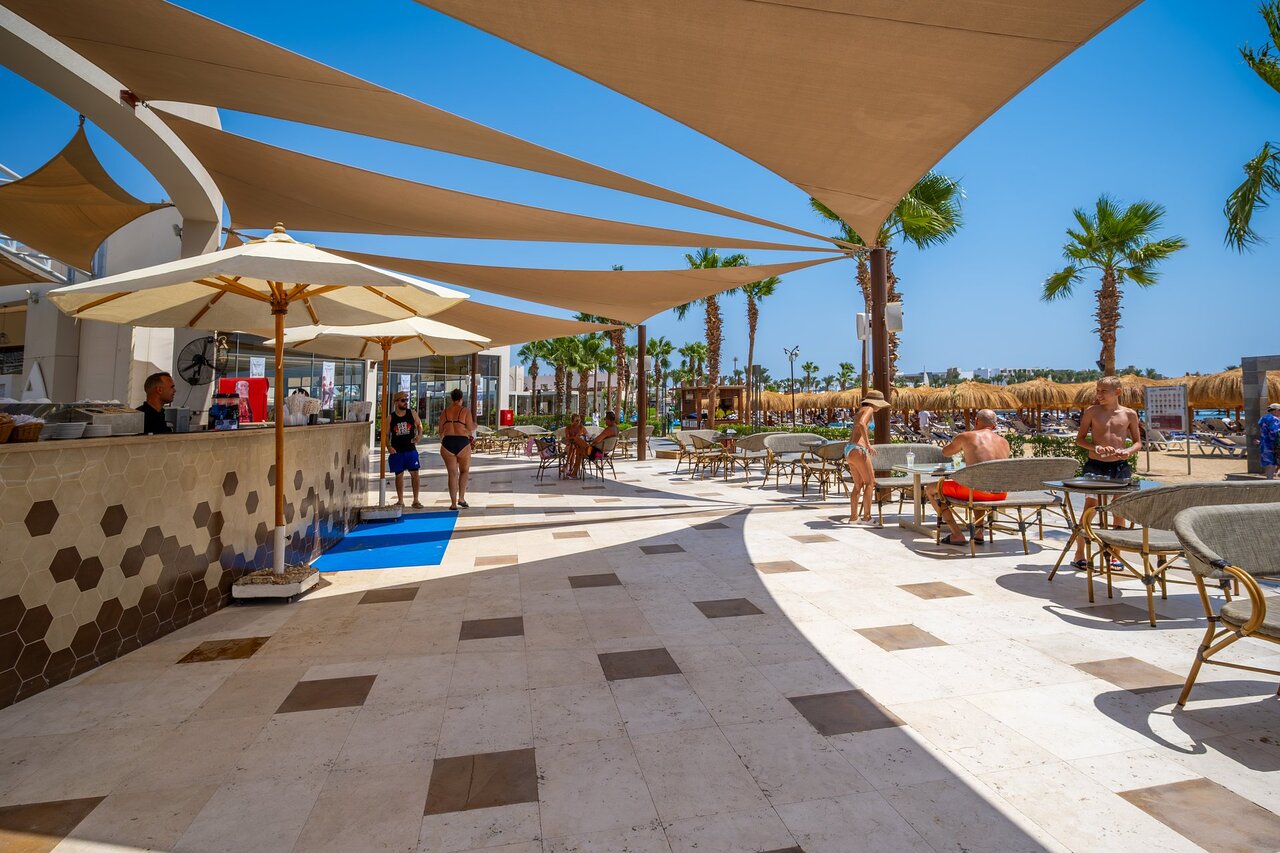 Atpūtas zona Xanadu Club Makadi Bay pie baseina ar saulessargiem un palmām.