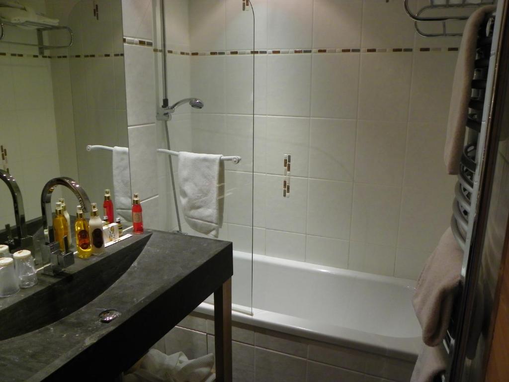 Mūsdienīga vannas istaba ar melnu akmens izlietni, dušu un vannu. Uz izlietnes novietotas dažādas higiēnas preces un dvieļi.