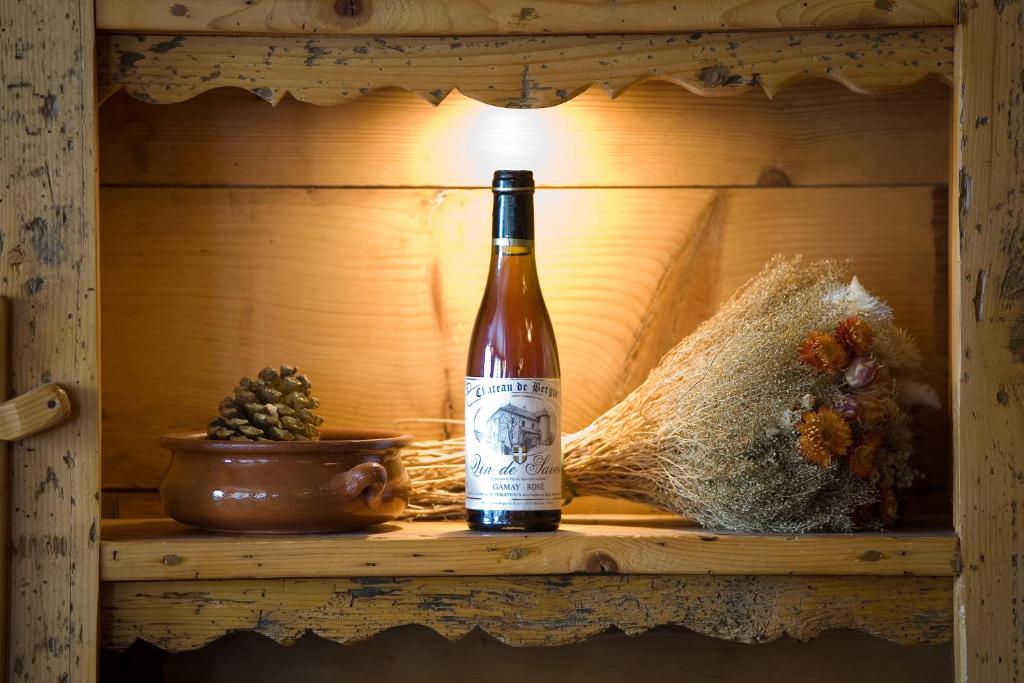 Plauktā novietota pudele ar vīnu, keramikas trauks un žāvētu ziedu pušķis, radot siltu un mājīgu atmosfēru.