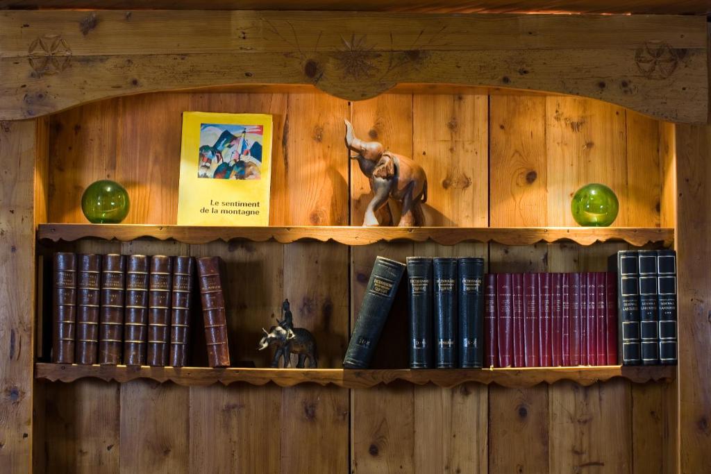 Koka grāmatplaukts ar dažādām grāmatām, dekoratīviem elementiem un zaļu stikla bumbu, radot mājīgu atmosfēru. Redzama arī koka figūra, kas attēlo ziloņu.