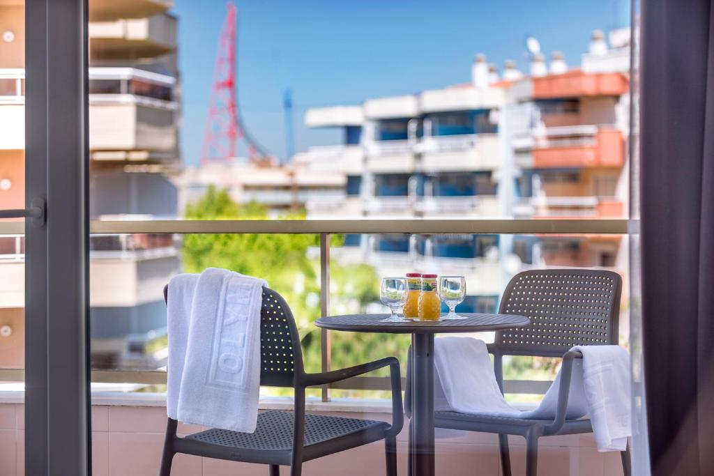 Balkona skats ar divām krēslām, galdu un dzērieniem, kas iedvesmo relaksāciju. Fons veido modernas ēkas un zaļo dabu.