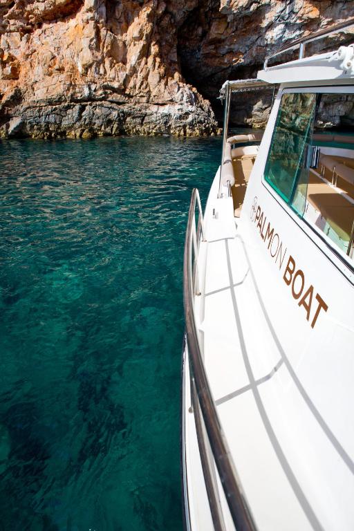 Lieliska jahta "Salmon Boat" peldoša skaidrā ūdenī, ar klints fona, kas rada gleznainu ainavu.